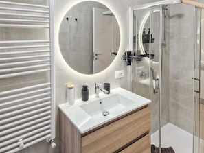 Een moderne badkamer met een witte wastafel, een ronde spiegel en een douchecabine van glas.