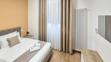 Et hotelværelse med seng, gardiner, en radiator og et sengebord.