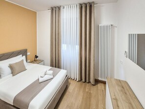 Ein Hotelzimmer mit Bett, Vorhängen, Heizkörper und Nachttisch.