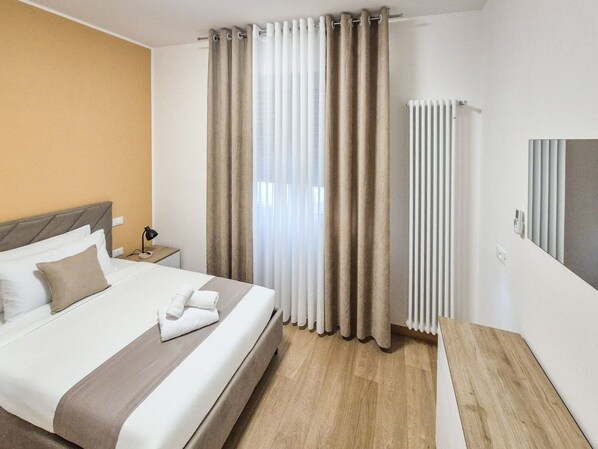 A hotel room with a bed, curtains, a radiator, and a bedside table. - defaultName (Vicenza)