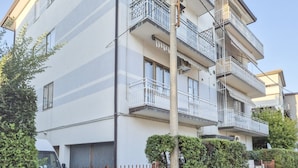 Un edificio residenziale a più piani con balconi, un ingresso carrabile e cielo sereno.