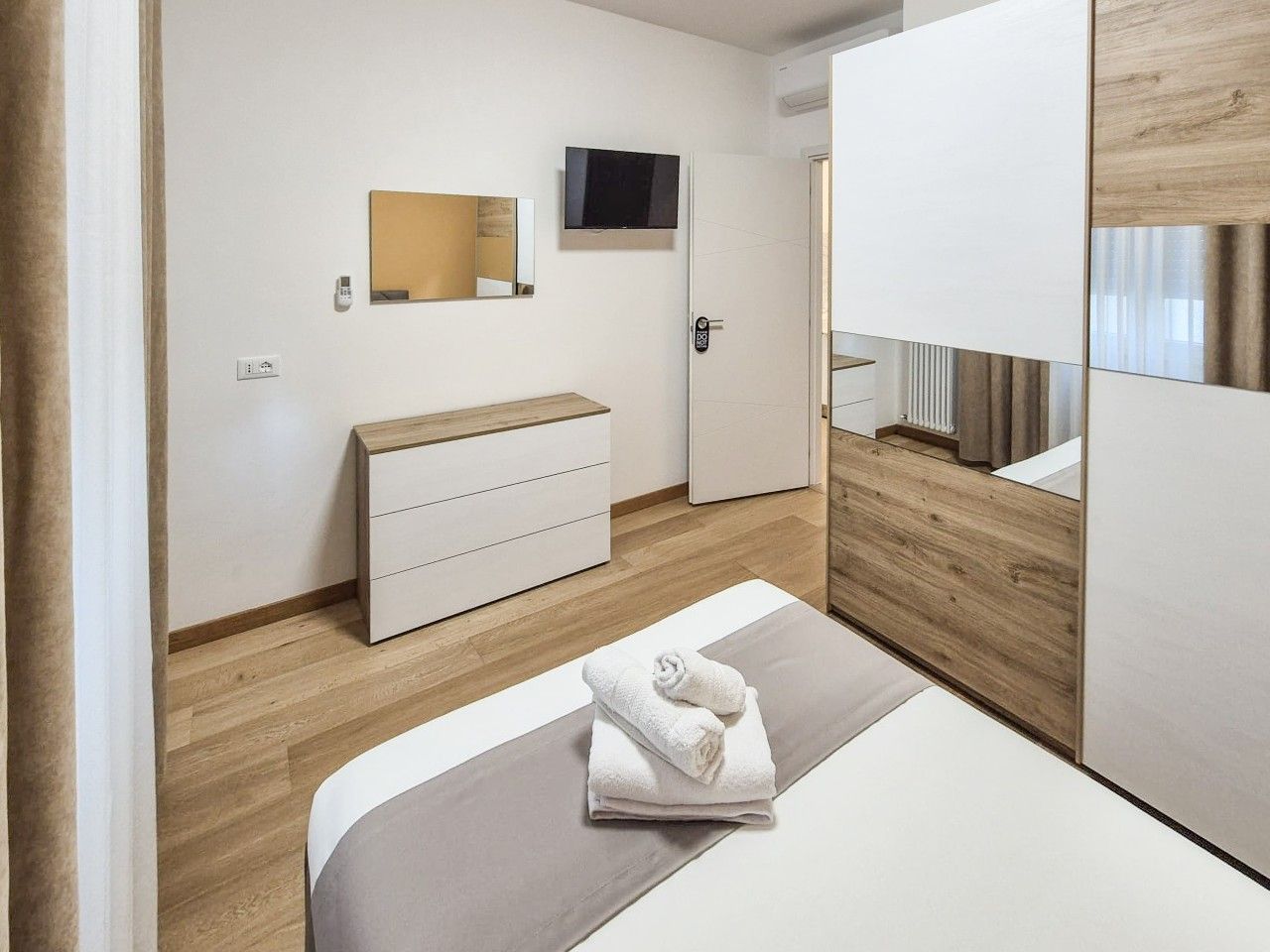 Et moderne hotelværelse med en seng, en trækommode, et fjernsyn ophængt på væggen og en dør med digital lås.