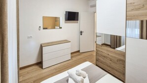 Habitació d'hotel moderna amb un llit, un taulell de nit de fusta, una televisió penjada a la paret i una porta amb tancament digital.