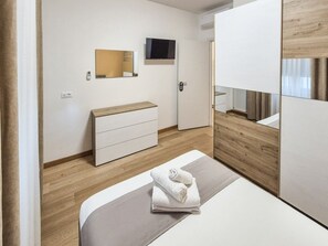 A modern hotel room with a bed, a wooden dresser, a television mounted on the wall, and a door with a digital lock. - defaultName (Vicenza)