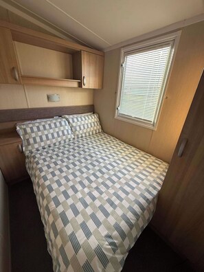Un dormitorio de autocaravana con cama, ventana con persianas y armarios de madera integrados.