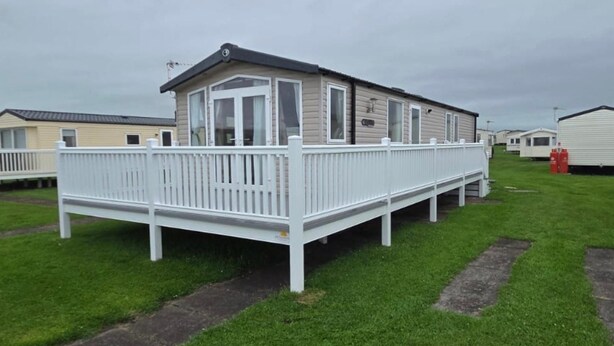A mobile home with a fenced deck, surrounded by grass and other similar homes.
