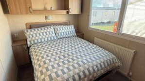 A bedroom with a bed, a nightstand, a built-in wooden cabinet, a window with blinds, and a radiator.