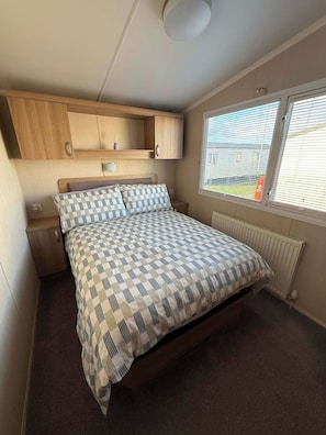A bedroom with a bed, a nightstand, a built-in wooden cabinet, a window with blinds, and a radiator.
