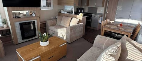 A compact living space with a sofa set, a coffee table, a flat-screen TV, and a kitchen area with a stove and microwave.
