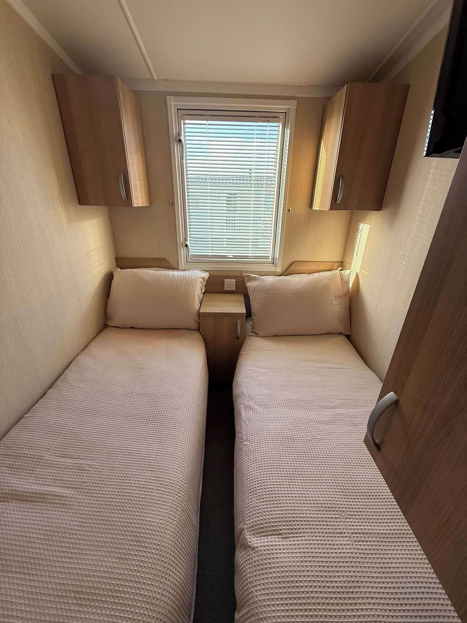 Ein kompaktes Wohnmobil-Interieur mit zwei Betten, einem Fenster und Holzausbau.