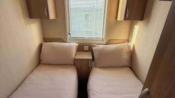 A compact RV interior with two beds, a window, and wooden cabinets.