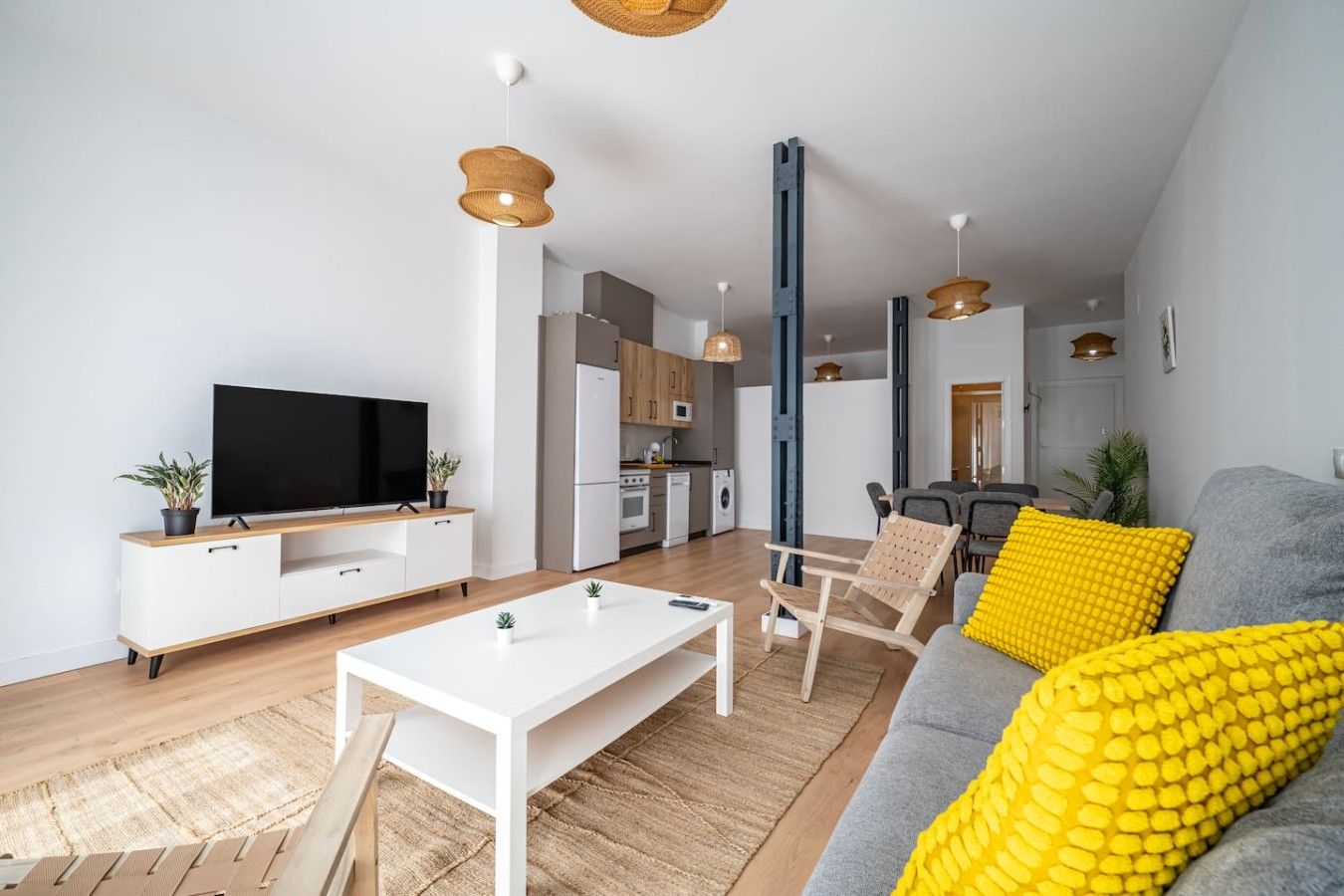 En moderne stue med et fladskærms-tv, et hvidt sofabord og en grå sofa med gule puder.