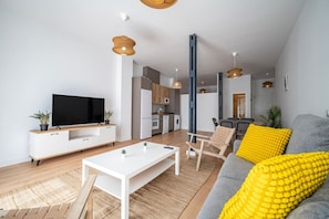 En moderne stue med et fladskærms-tv, et hvidt sofabord og en grå sofa med gule puder.