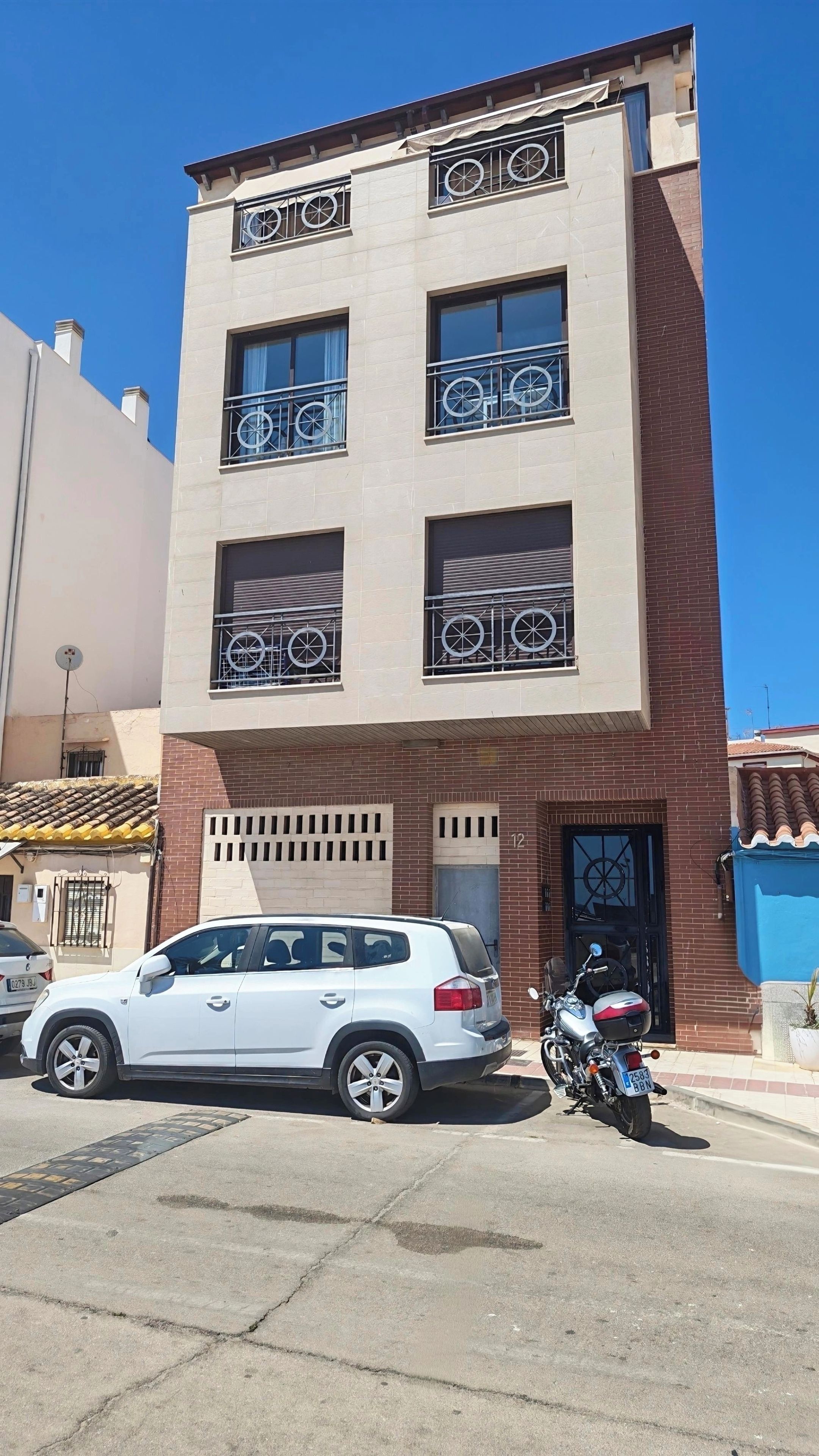 Edifício de vários andares com varanda, um carro e uma motocicleta estacionados na frente.