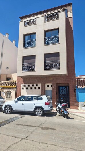 Edifício de vários andares com varanda, um carro e uma motocicleta estacionados na frente.