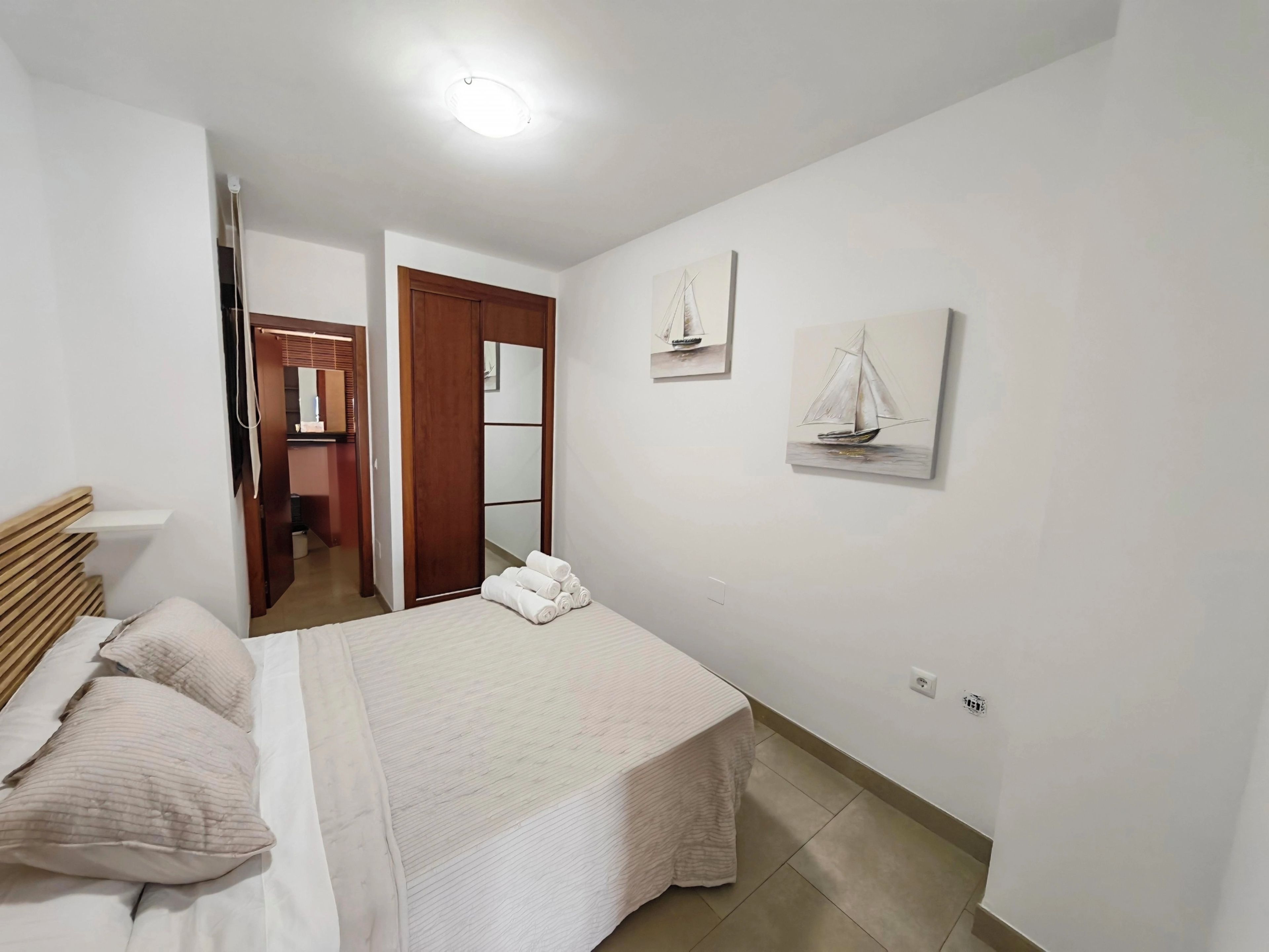 Quarto com cama, travesseiros, mesa de cabeceira, espelho e obras de arte na parede.
