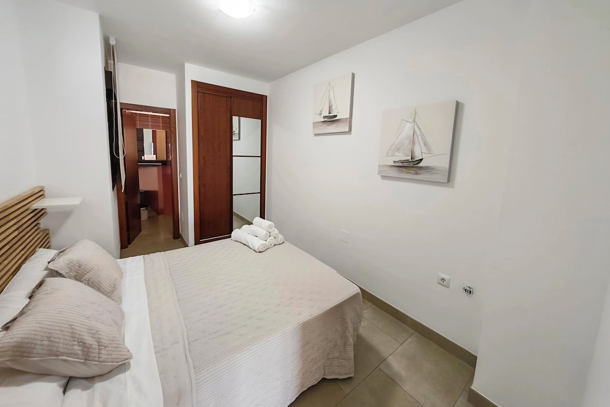 Quarto com cama, travesseiros, mesa de cabeceira, espelho e obras de arte na parede.