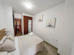 A bedroom with a bed, pillows, a bedside table, a mirror, and artwork on the wall.