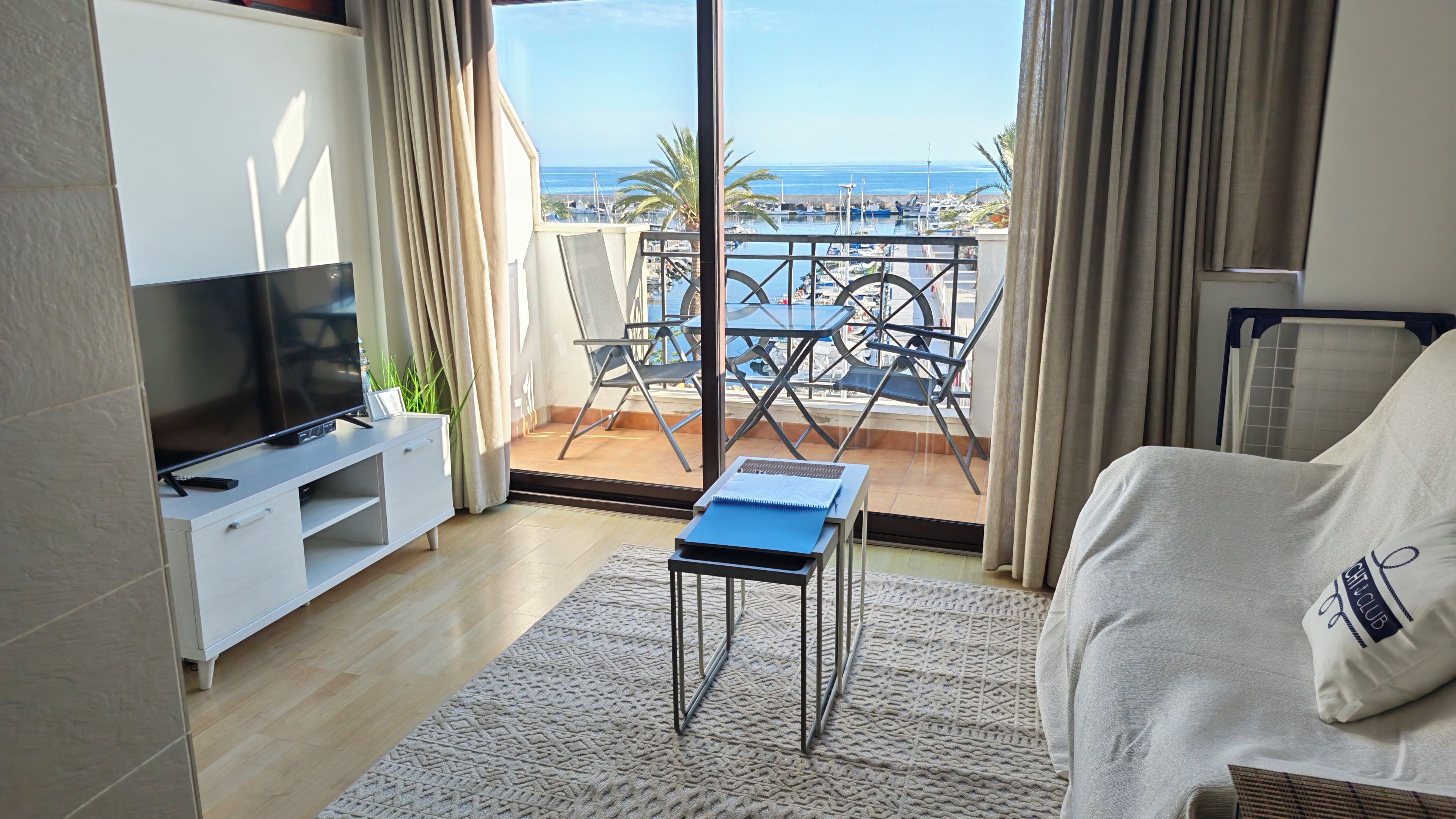 Une chambre d’hôtel moderne dotée d’un balcon, d’une télévision à écran plat, d’un canapé et d’une petite table avec un carnet.