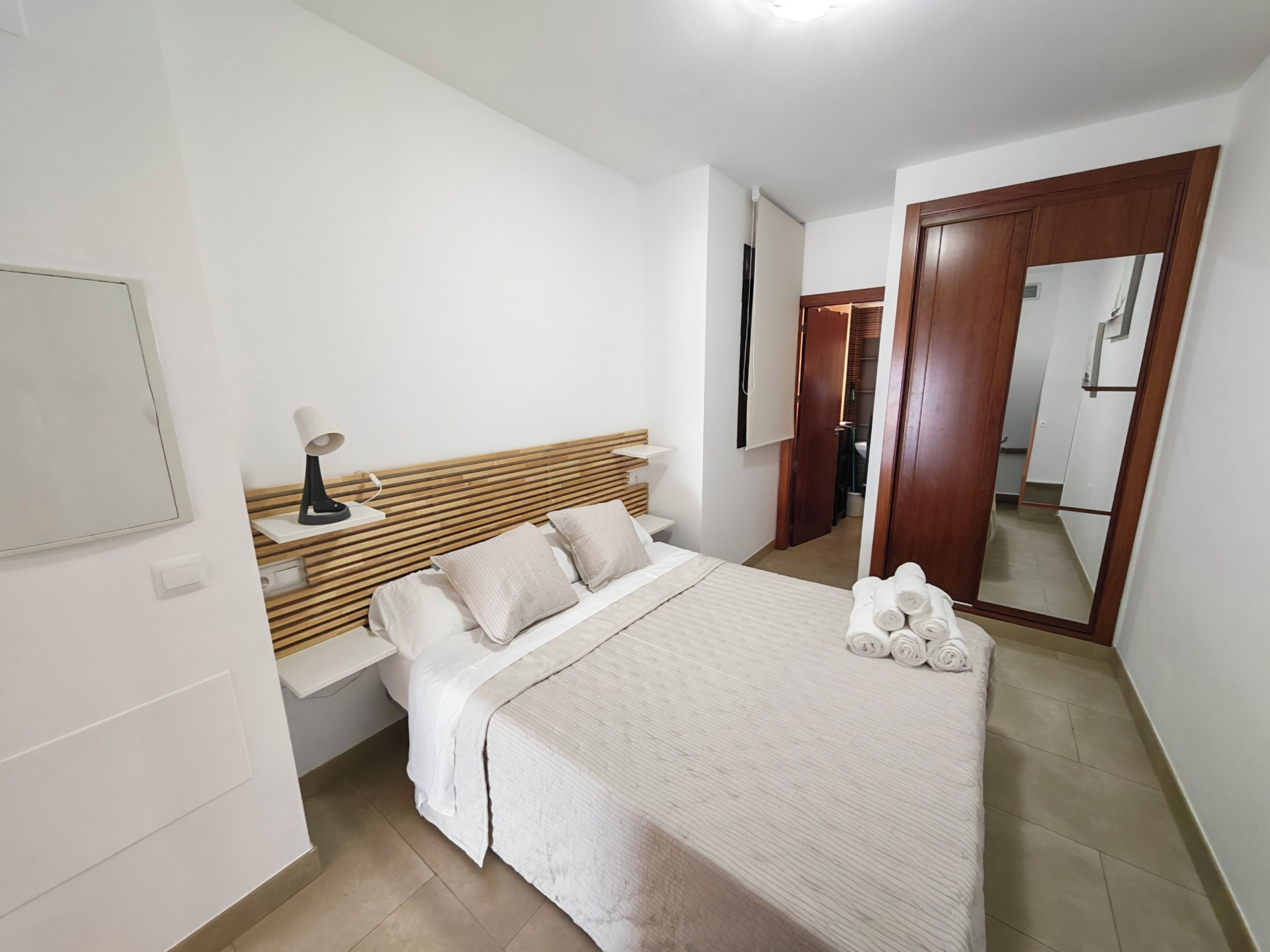 Quarto com cama, mesa de cabeceira, abajur e espelho.