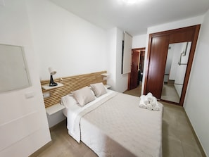 Quarto com cama, mesa de cabeceira, abajur e espelho.