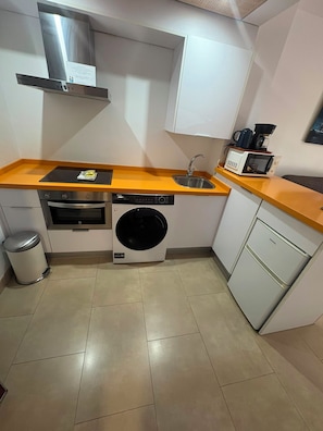 Cozinha compacta com fogão de aço inoxidável, máquina de lavar embutida, micro-ondas e uma pia pequena.