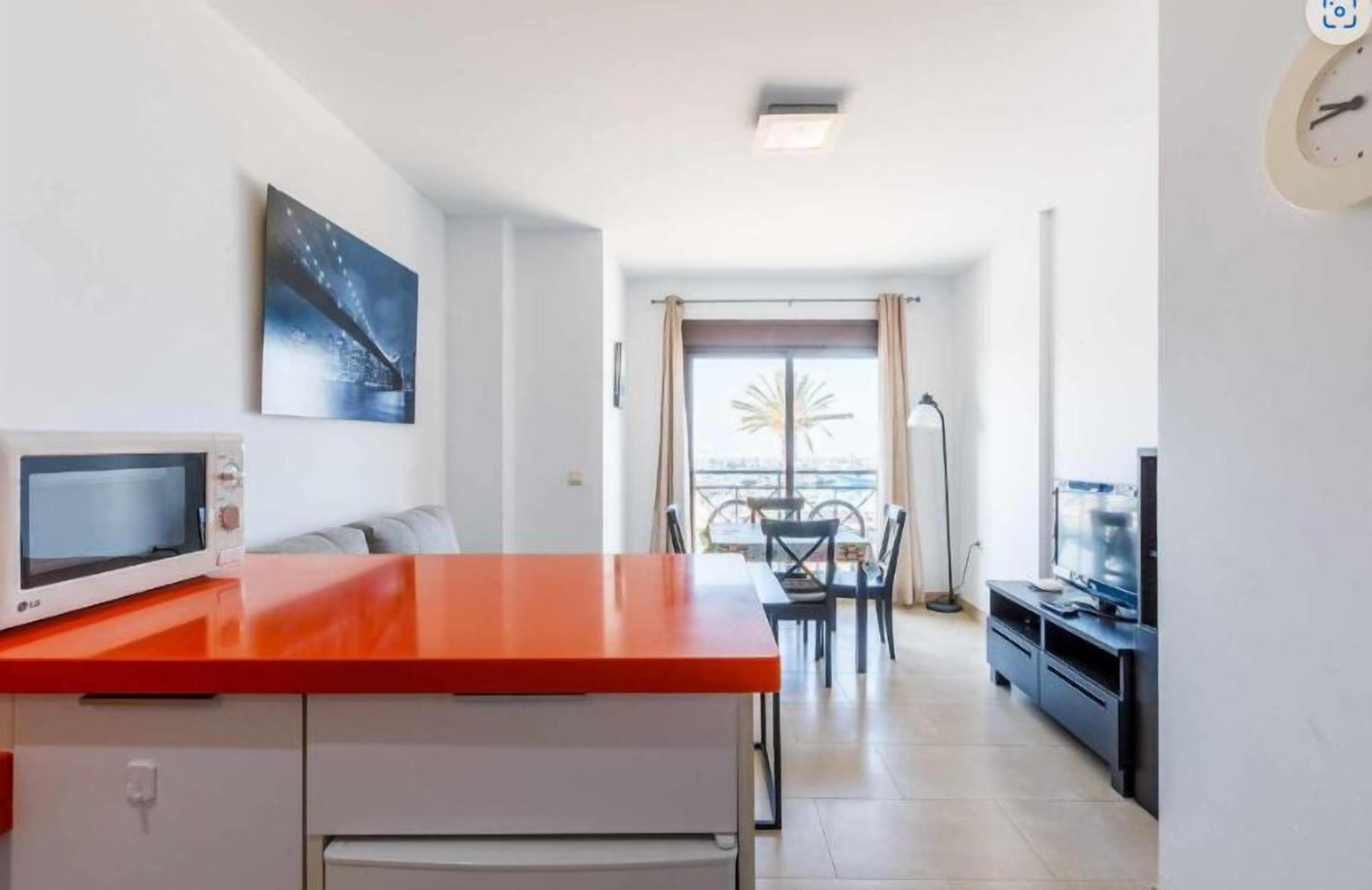 Une cuisine moderne avec un plan de travail rouge, un four à micro-ondes et un coin repas comprenant une table et des chaises.