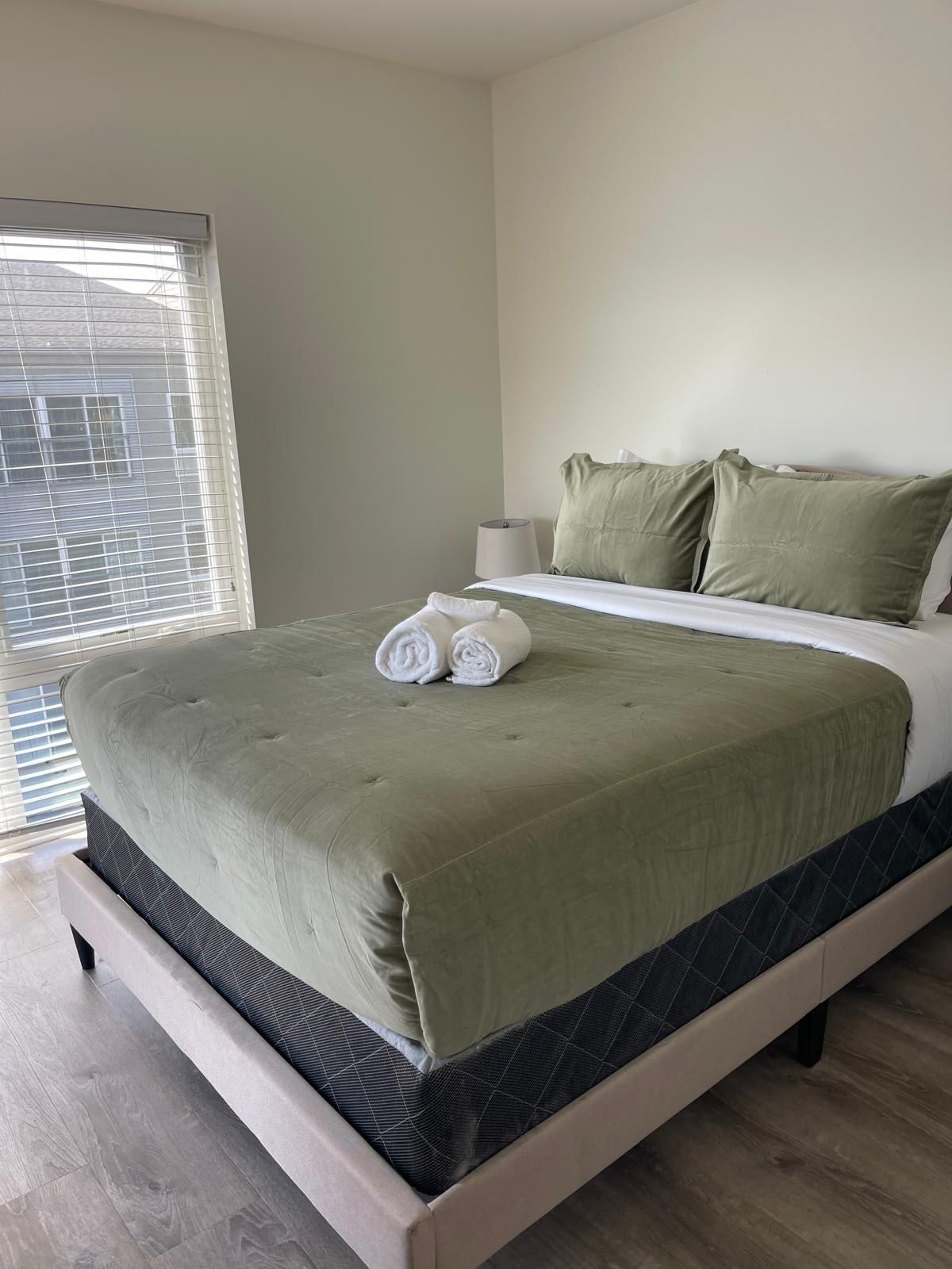 A neatly made bed with a green bedspread, two pillows, and rolled white towels.