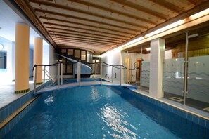 An indoor swimming pool with a wooden ceiling, glass railings, and tiled walls.