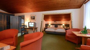Ett hotellrum med ett träpanelat tak, en säng med sänggavel, två stolar, ett litet bord och en tv som står på ett skrivbord.