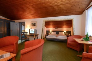 Une chambre d’hôtel avec un plafond en bois, un lit avec une tête de lit, deux chaises, une petite table et un téléviseur posé sur un bureau.