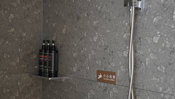 Ducha con cabezal de ducha manual y panel de control en la pared. Señal de precaución que indica suelo resbaladizo.