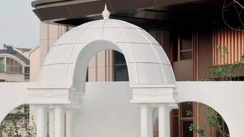 Entrada de hotel con un arco blanco y columnas, un letrero con el nombre del hotel, y una persona parada frente a él.