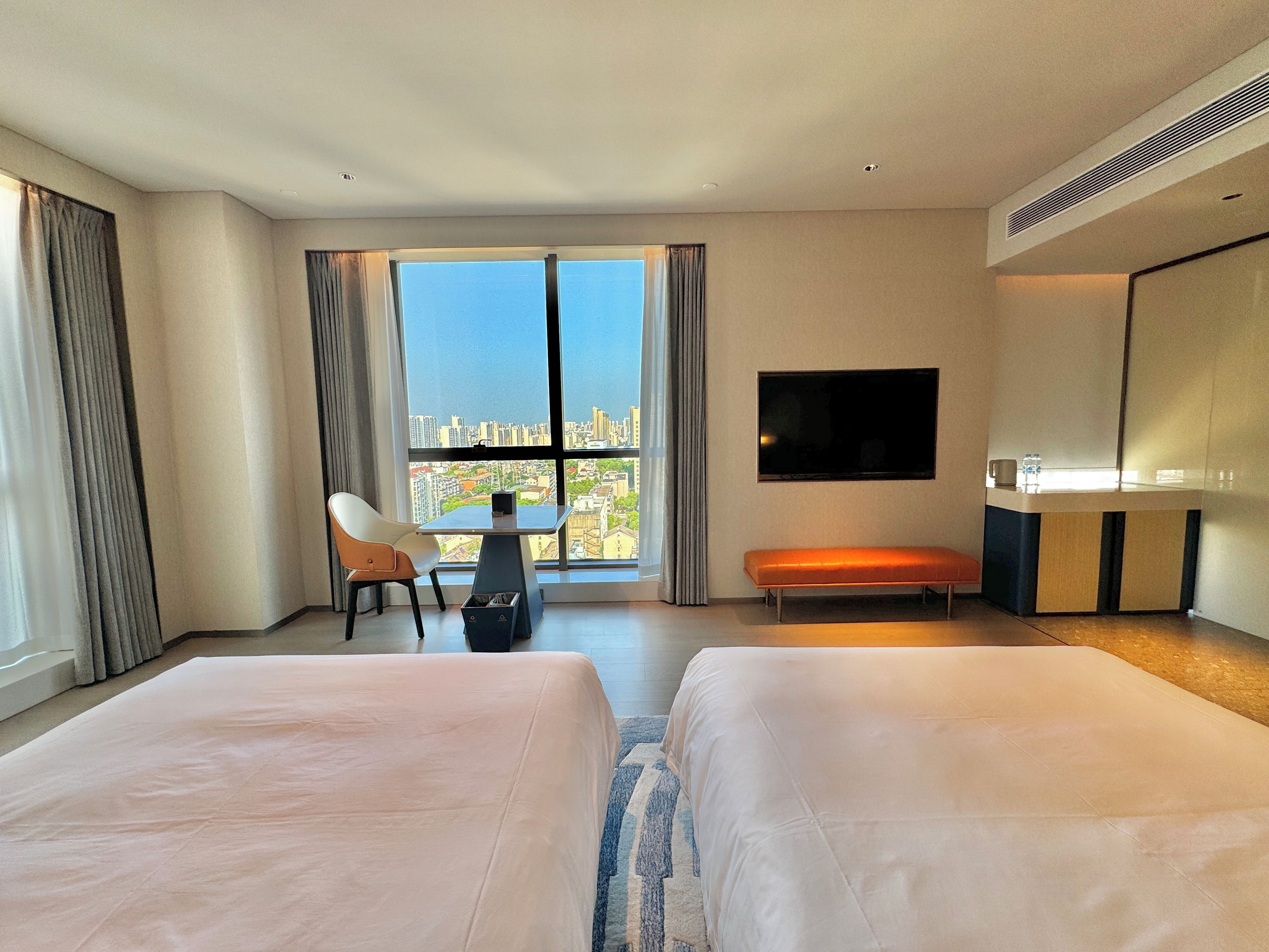 Habitación de hotel con dos camas, un escritorio, una silla, un televisor y vistas a la ciudad.