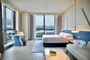 A modern hotel room with a large bed, a sitting area, and a view of the cityscape.