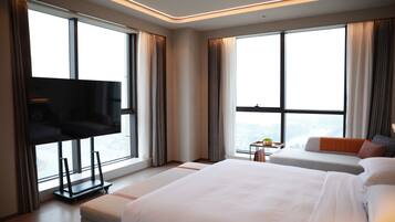 Habitación de hotel moderna con una cama grande, una cama más pequeña, un televisor y vistas a la ciudad.