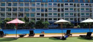 A hotel pool area with lounge chairs, umbrellas, and a building with balconies in the background. - Room-top Floor Duplex With High Ceiling (Pattaya)
