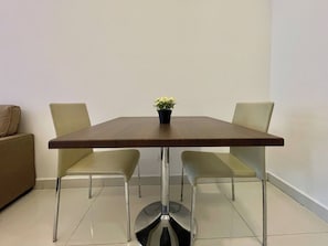 A dining table with four chairs, a potted plant, and a sofa in a room with plain walls and tiled flooring. - Room-top Floor Duplex With High Ceiling (Pattaya)