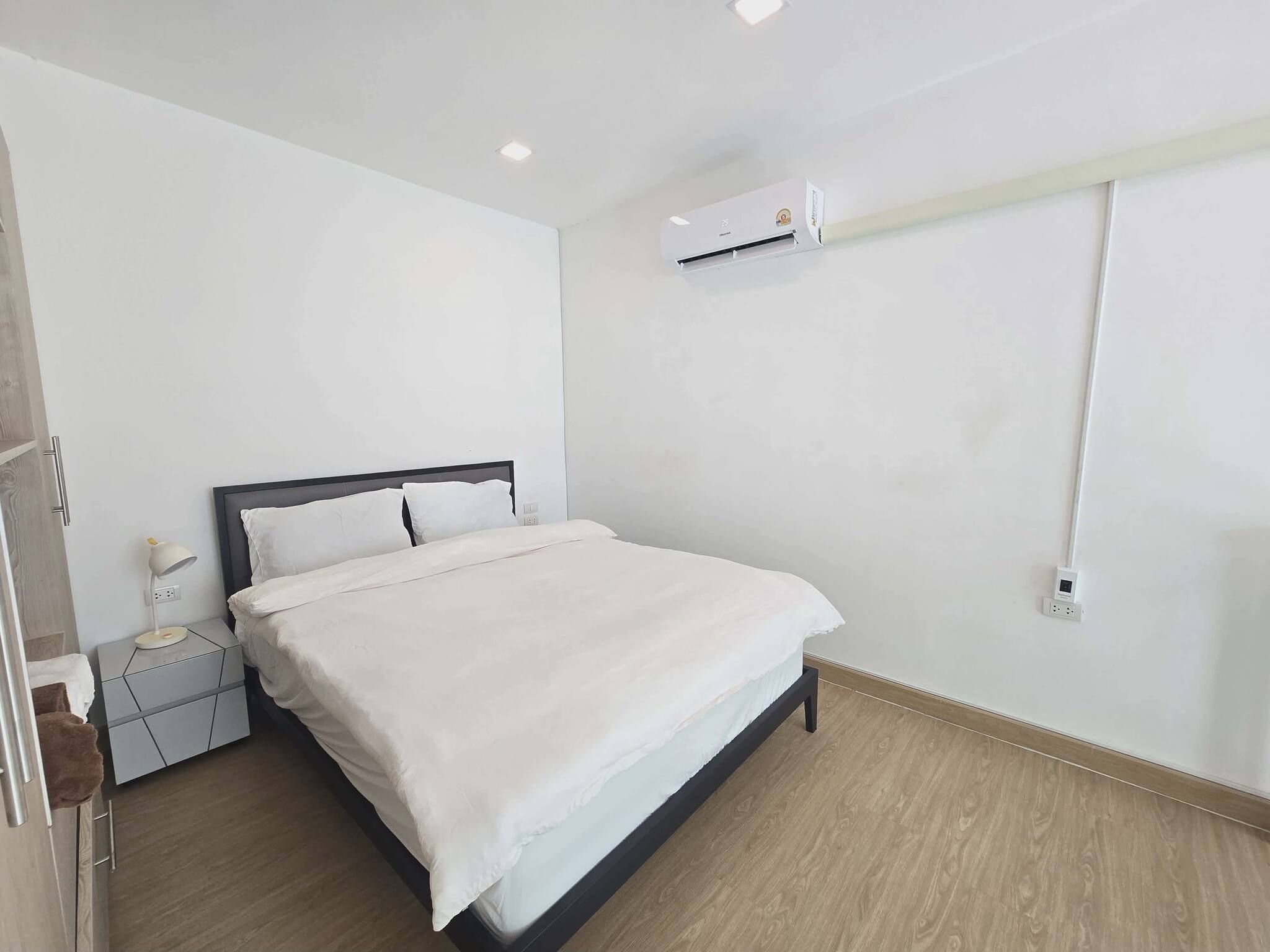 A modern bedroom with a bed, bedside table, lamp, and an air conditioning unit.