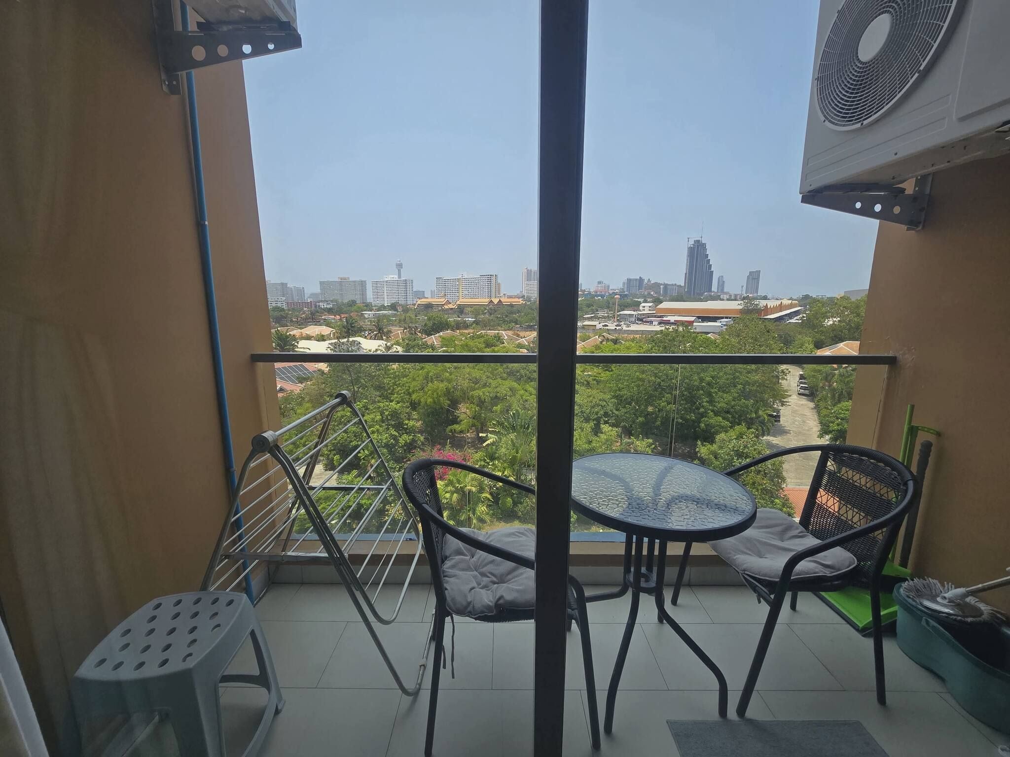 A balcony with a table and chairs, a view of a cityscape, and a fan.