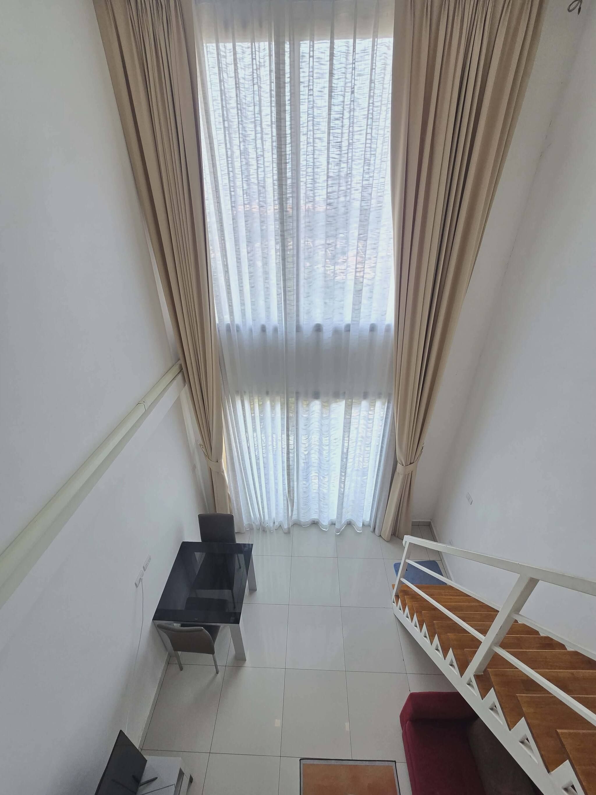 Una habitación con vistas, cortinas translúcidas, una mesa de comedor, sillas y una escalera.
