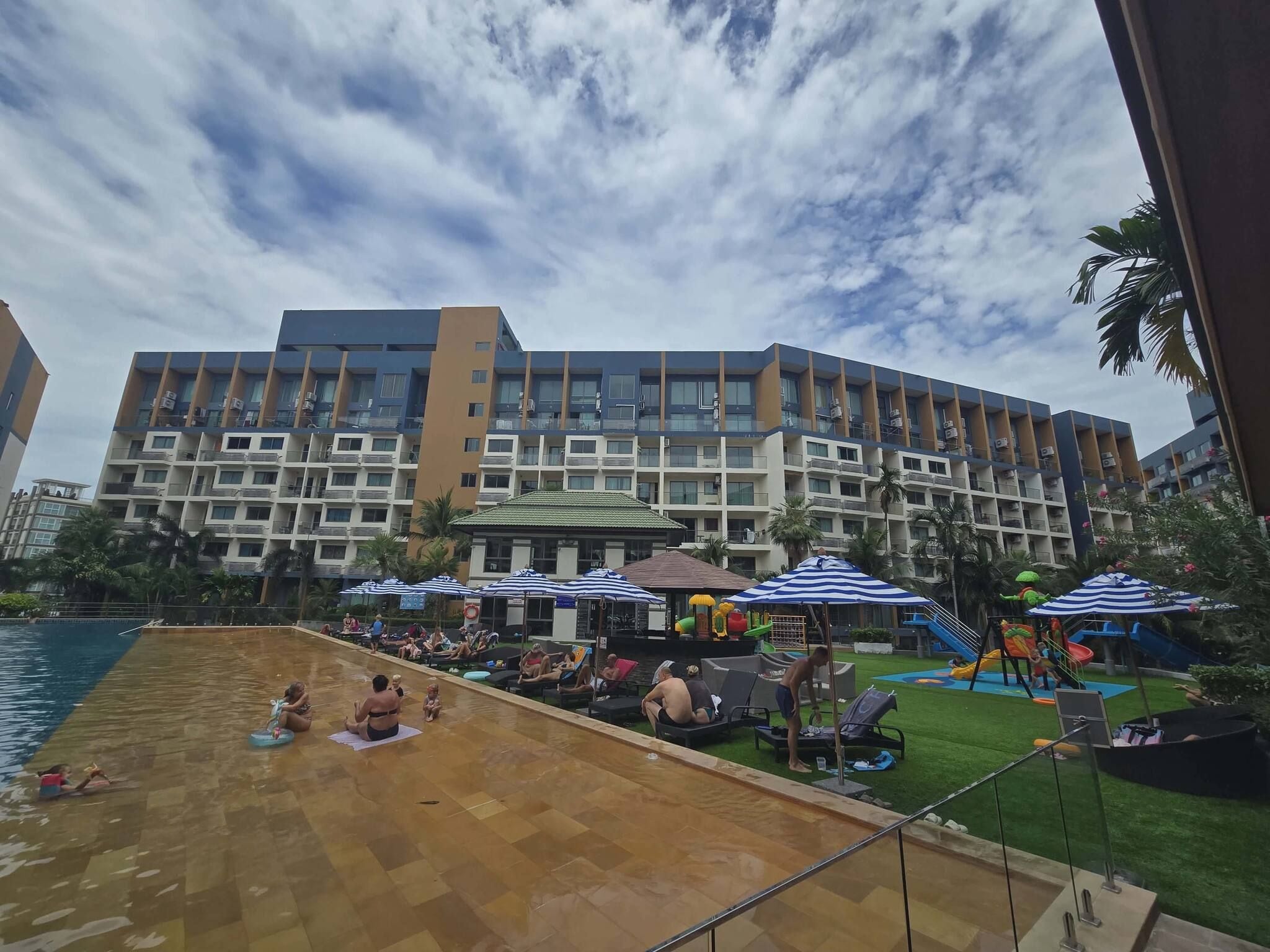 Un hotel con piscina, varios balcones y una zona de juegos infantiles.