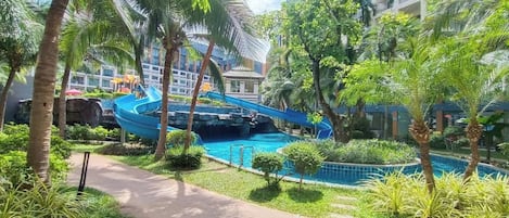 A pool area with a blue water slide, surrounded by palm trees and greenery.