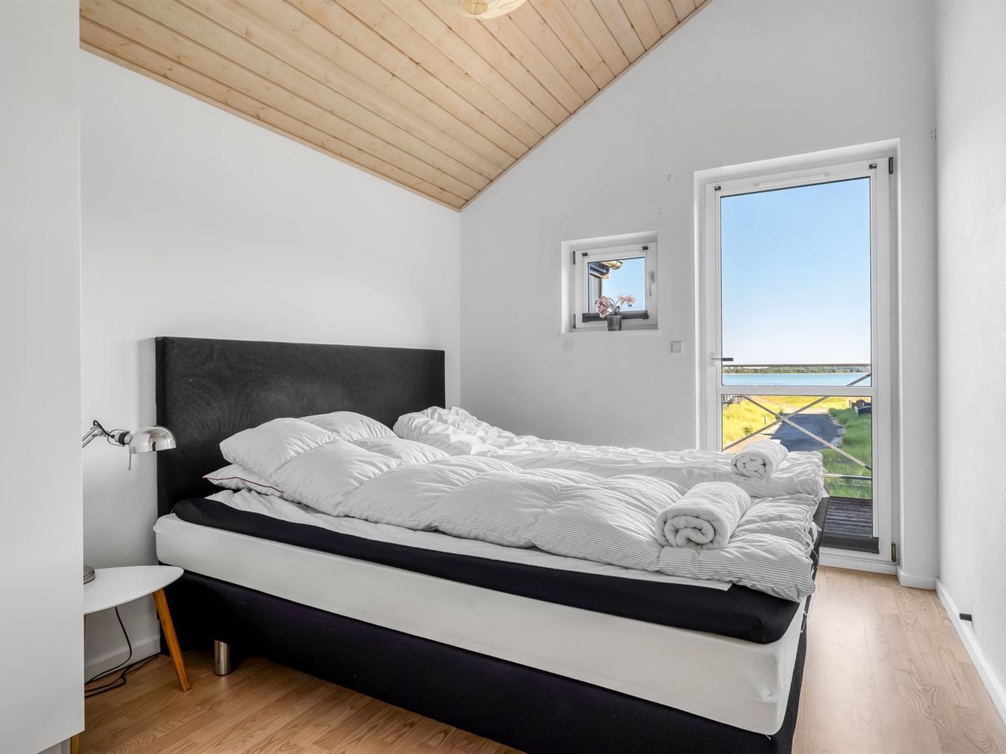 Un dormitorio con cama, mesita de noche, lámpara y vistas al exterior.