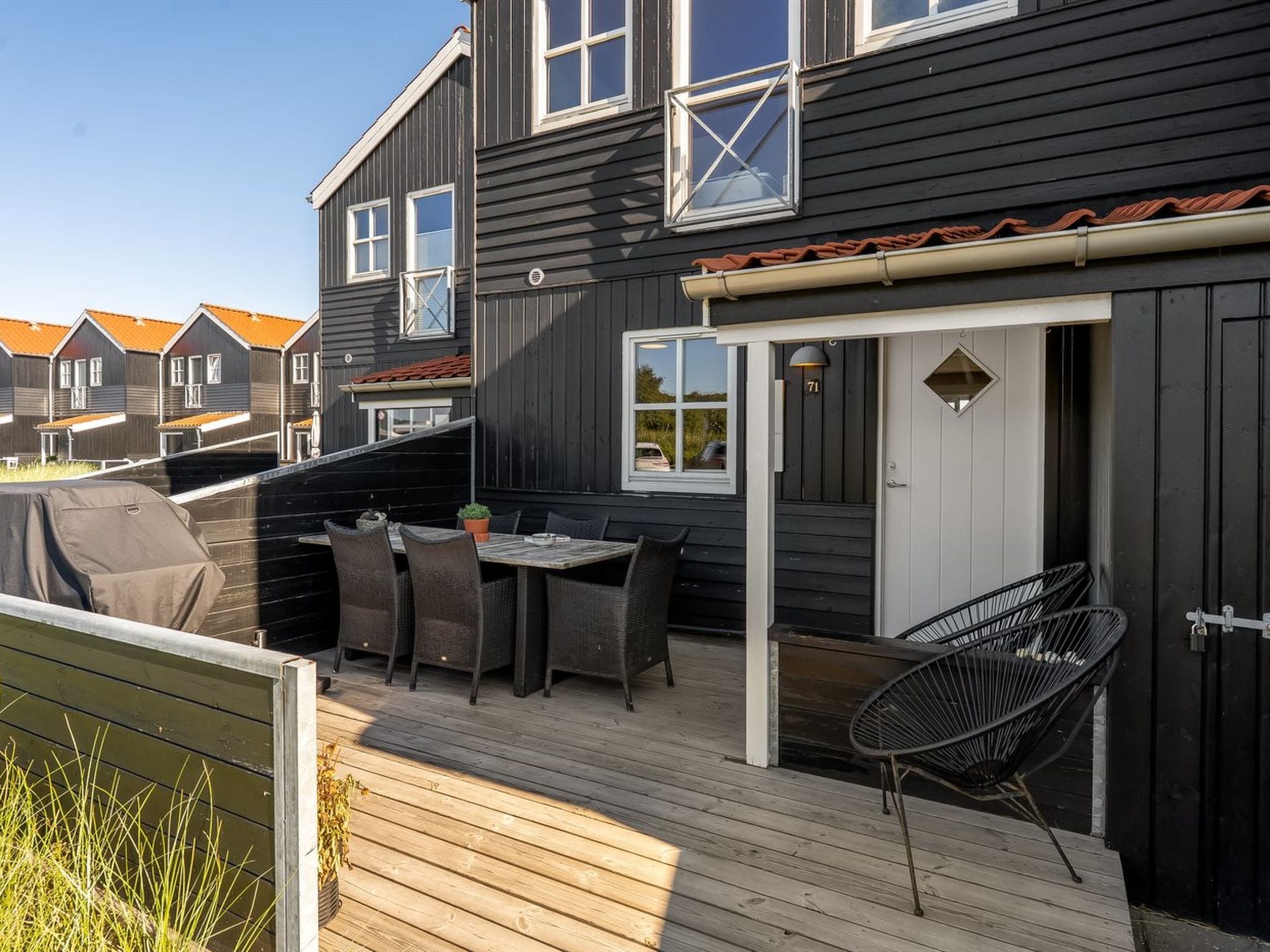 A deck with outdoor furniture, a grill, and a view of neighboring houses.