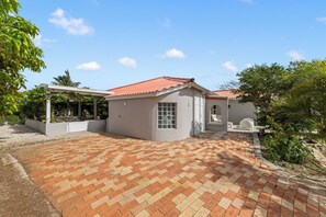 Ein Wohnhaus mit gepflasterter Terrasse, einem überdachten Sitzbereich und einem kleinen Gebäude mit rotem Ziegeldach.