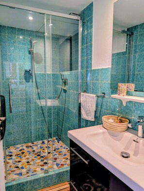 Ein Badezimmer mit einer Duschkabine, Fliesenboden, Waschbecken mit Spiegel und Handtuchhalter.