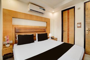 A hotel room with a large bed, wooden headboard, bedside table with lamp, and a door with a wooden panel. - Hotel O Vintage (New Delhi)