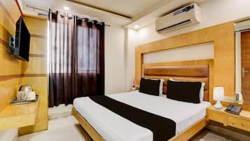 A hotel room with a bed, bedside table, lamp, phone, and an air conditioning unit.