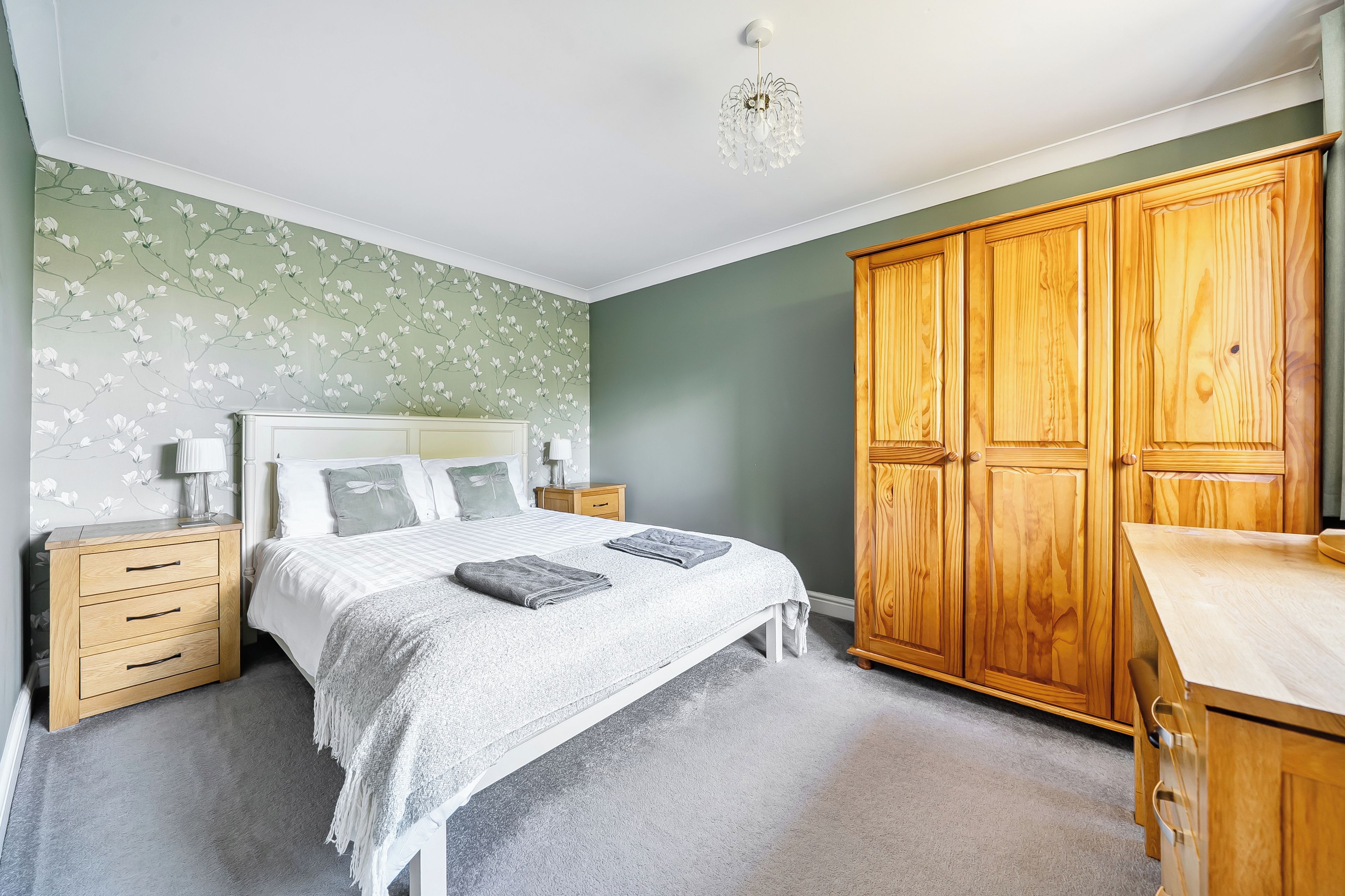 A bedroom with a bed, nightstands, a wooden wardrobe, and a chandelier.